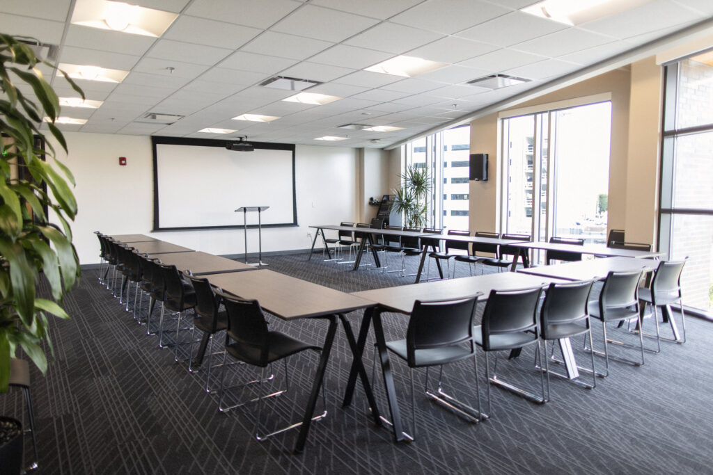 Edgewood event space at CIC Providence with tables and chairs in a U-shape, projector screen down at the front of the room, podium, and large windows.