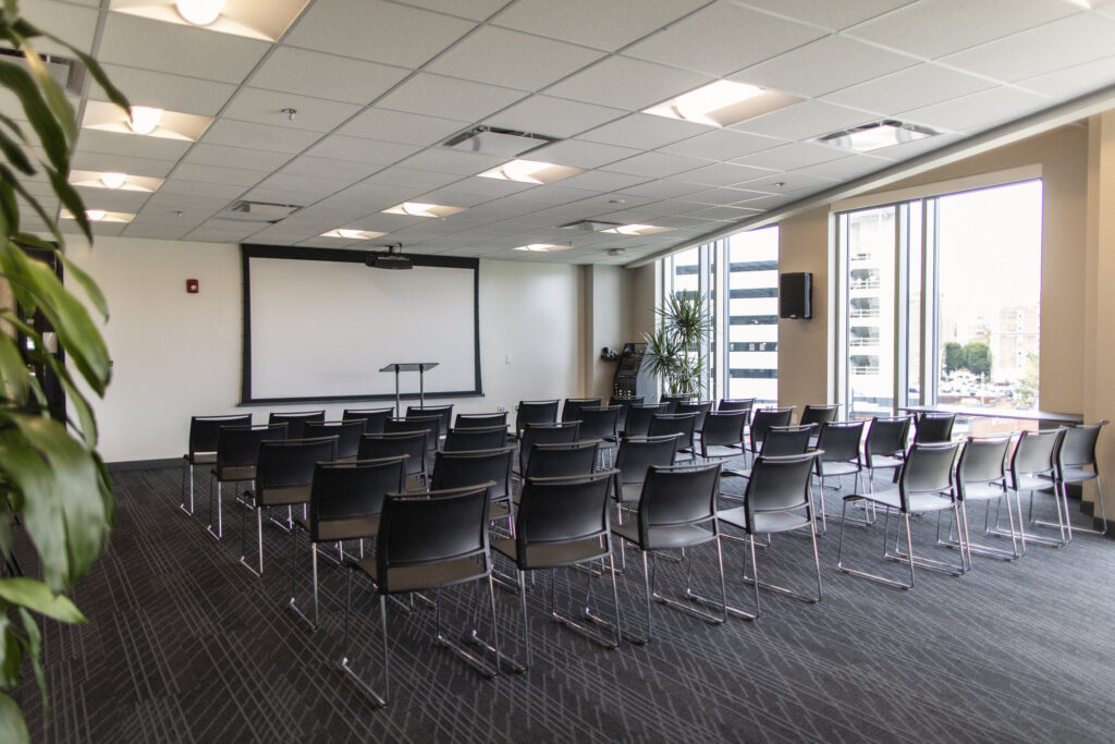 Edgewood event space at CIC Providence with chairs in lecture style, projector screen down at the front of the room, podium, and large windows.