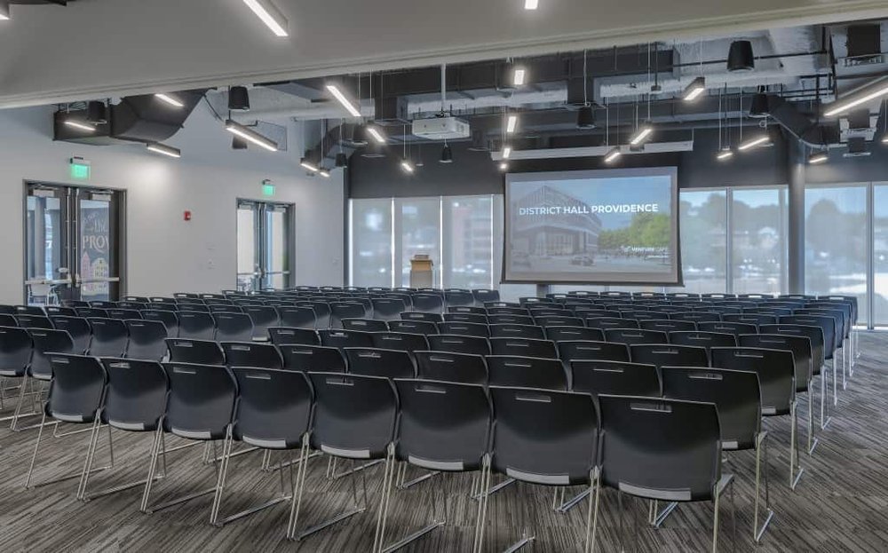 Full Assembly event space at CIC Providence with natural light, chairs in lecture style, and projector screen and podium at the front of the room