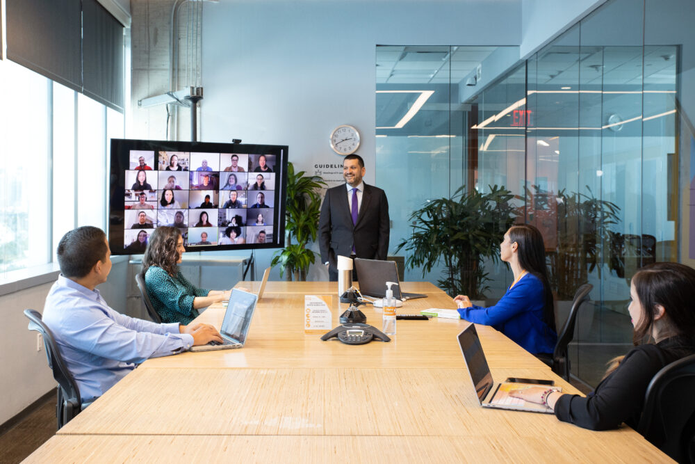 People collaborate in an office and virtually via a large screen
