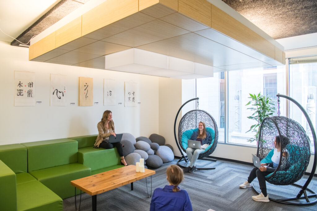 An example of how satellite offices benefit employees through inspiration. Four people talking while sitting in a modern and sleek workspace.