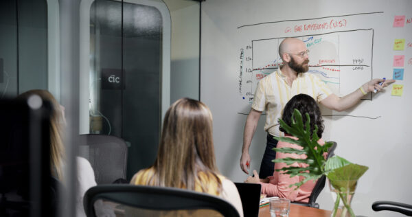 A man leading a facilitated whiteboard session in a conference room while several people listen