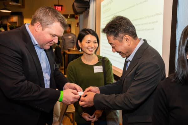 Three people talking in front of a screen at a networking event.